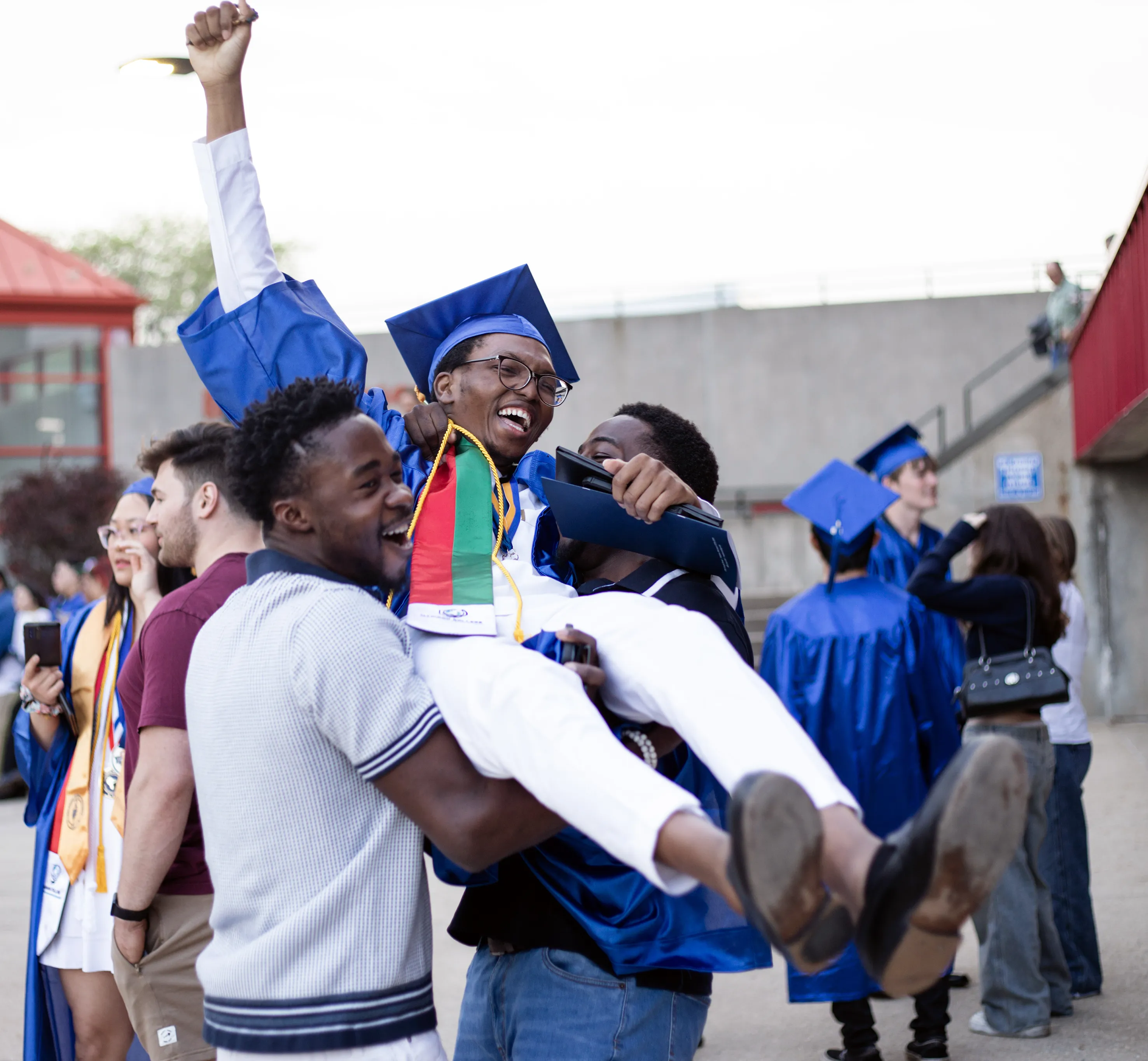 Graduate being held up in the air by two friends in celebration.