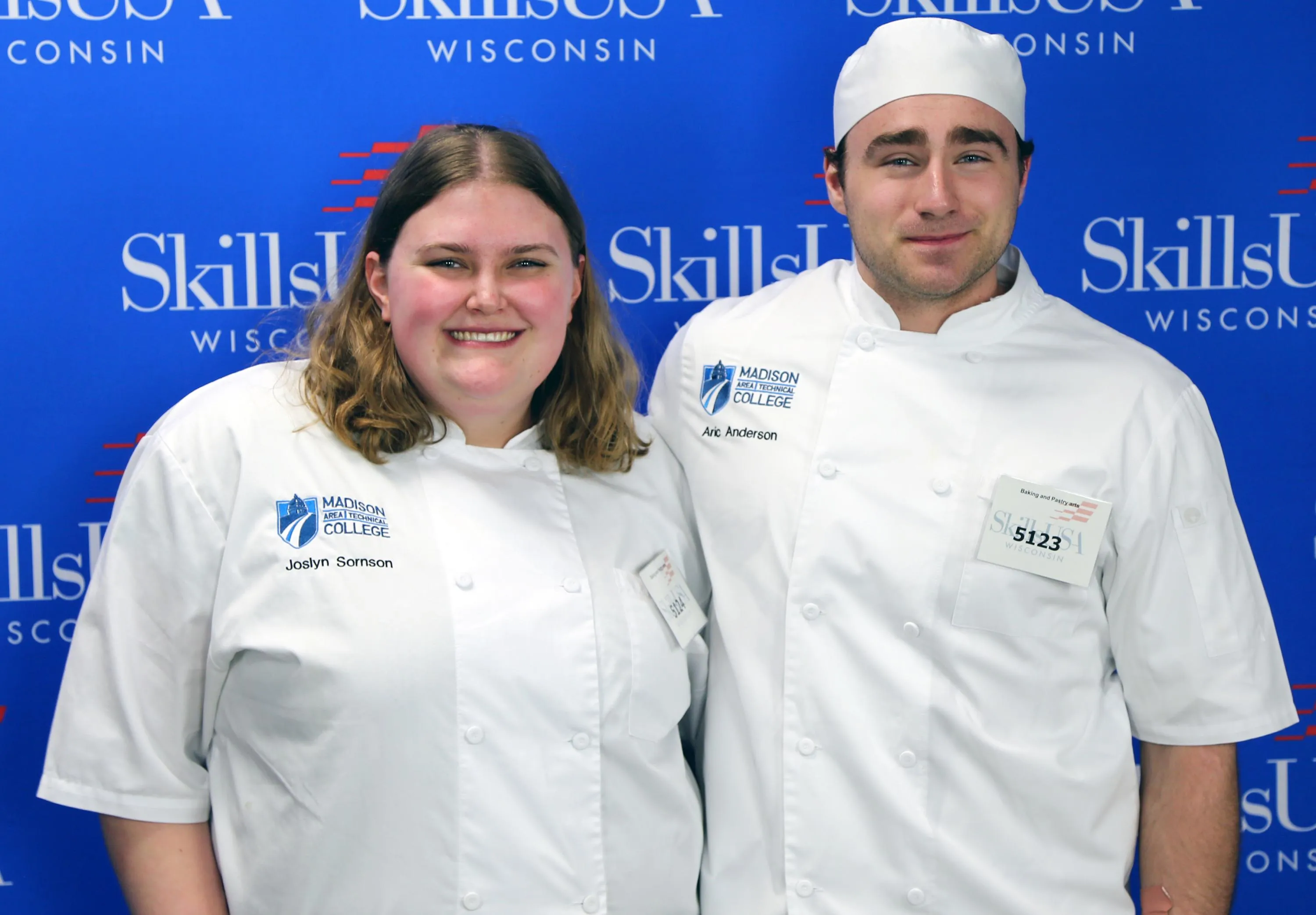 Joslyn Sornson adn Aric Anderson pose wearing white chef shirts in from of the SkillsUSA logo.