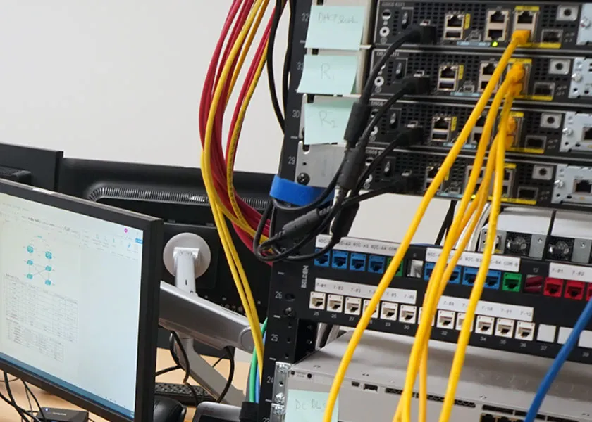 computer monitor with Cisco configuration on screen next to a server stack