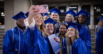 Image of Madison College graduates in blue caps and gown posing for a selfie.