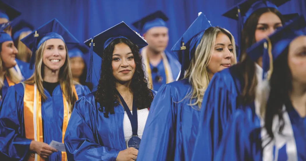 Photo of graduates coming into the 2025 Spring Commencement ceremony, wearing blue gowns and caps.