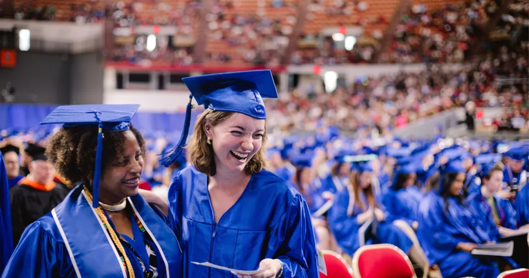 Photo of two Madison College students at commencement ceremony wearing blue cap and gowns.
