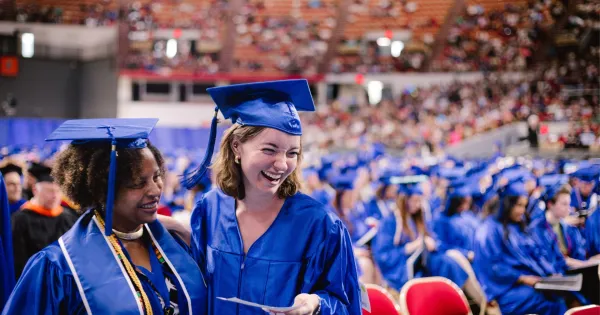 Photo of two Madison College students at commencement ceremony wearing blue cap and gowns.