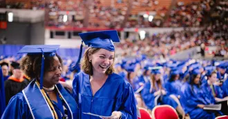 Photo of two Madison College students at commencement ceremony wearing blue cap and gowns.