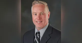 Portrait image of Bryan Woodhouse wearing a dark blazer and striped tie.