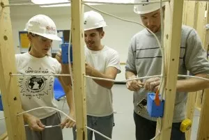 Three male students in hard hats roughing in insulated electrical wire in wood frame construction