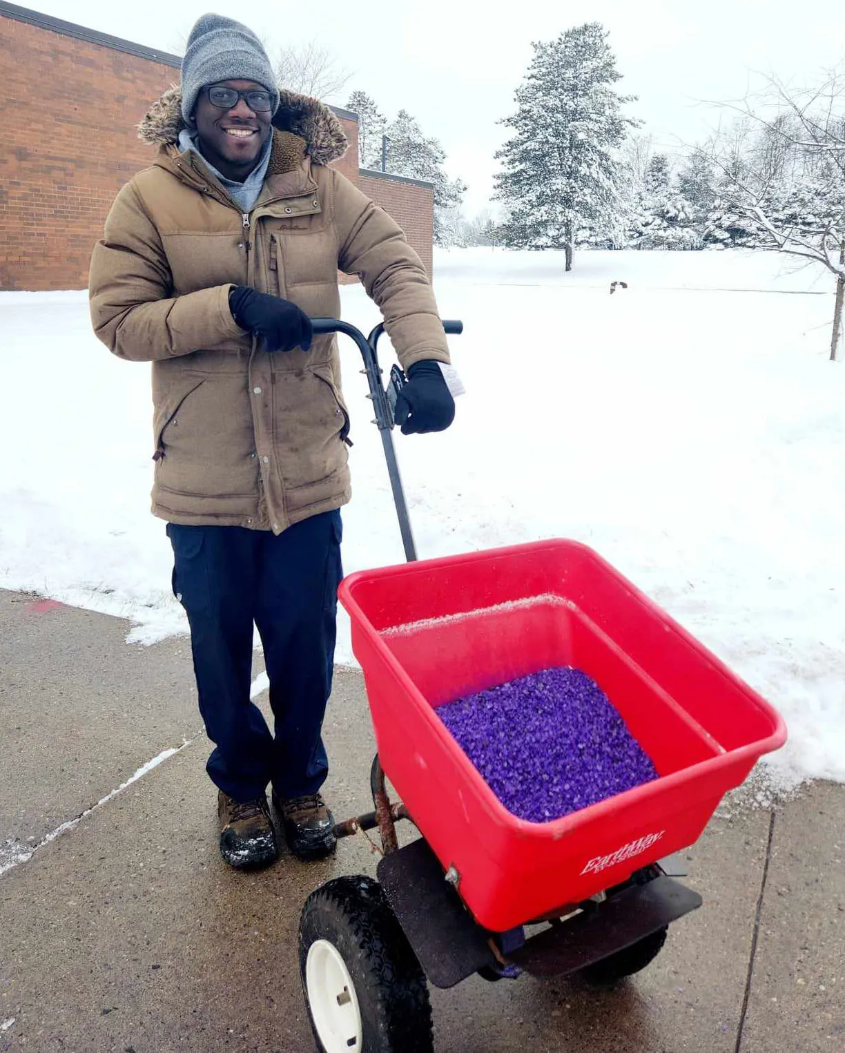 Madison College-Reedsburg Lead Custodian Franco Okello putting salt down on a sidewalk after a snow fall.