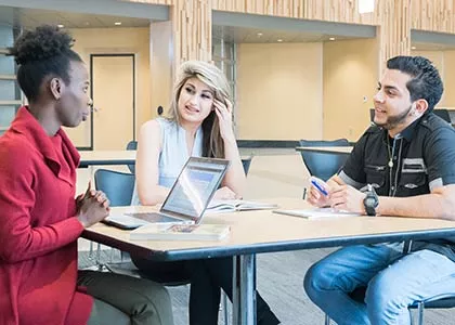 Three students seated at a table having a discussion.