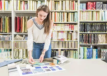 Student standing at table looking at a design in a room full of bookcases filled with design books.