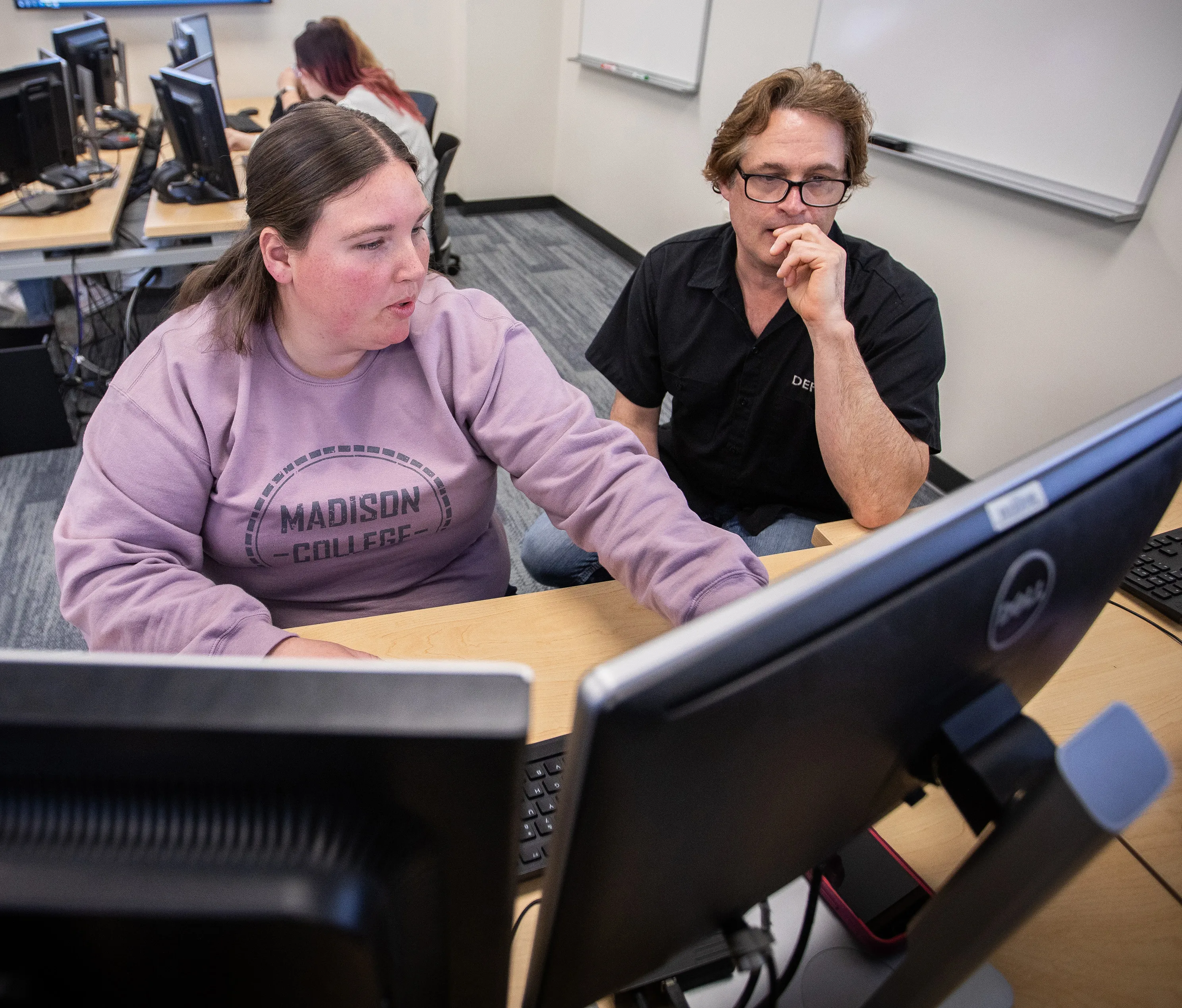 Student in class working on desktop computer with instructor by her side.