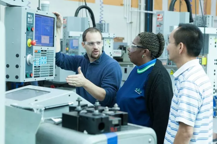 Instructor in industrial classroom standing at a control module providing explanation to two students