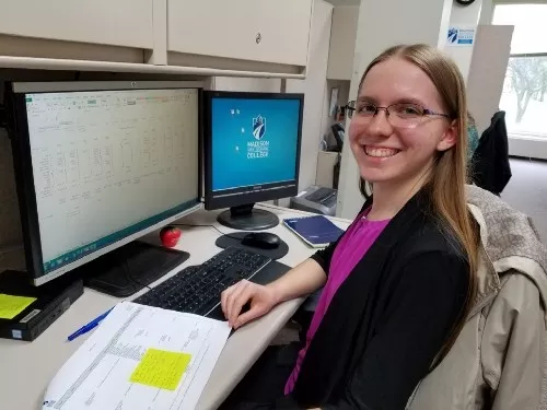 Jennifer Novey sits at a desk in front of computer monitors. 
