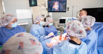 Students in blue scrubs and masks gathering around a simulated operating table, working on a patient manikin, as a instructor looks on.