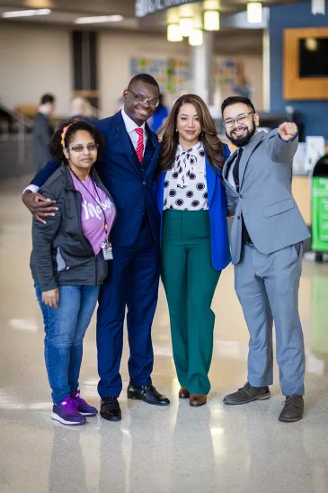 Four people smiling at camera. One of them is pointing.