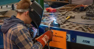 Welder, wearing a welder's hood, using a torch to weld material.