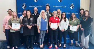 Madison College employees and community partners posing for a photo in front of a blue Madison College banner backdrop.