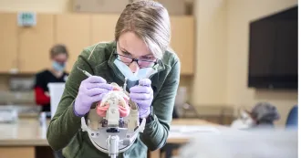 Dental students working on a set of simulated mouth and teeth in dental clinic lab.