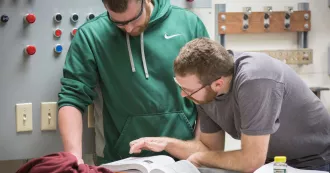 Two Madison College electricity program students looking at textbook.