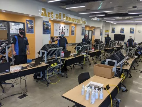 Students stand spaced apart in classroom while wearing masks.