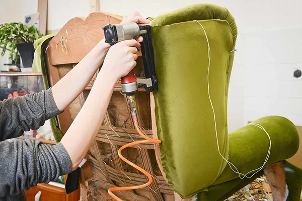 hands holding a staple gun, stapling fabric onto a green chair