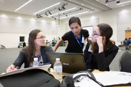 Three women look at a laptop. 