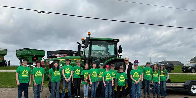 Students wearing matching green shirts standing infront of green tractors