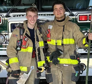 two people smiling at the camera in fire fighter gear