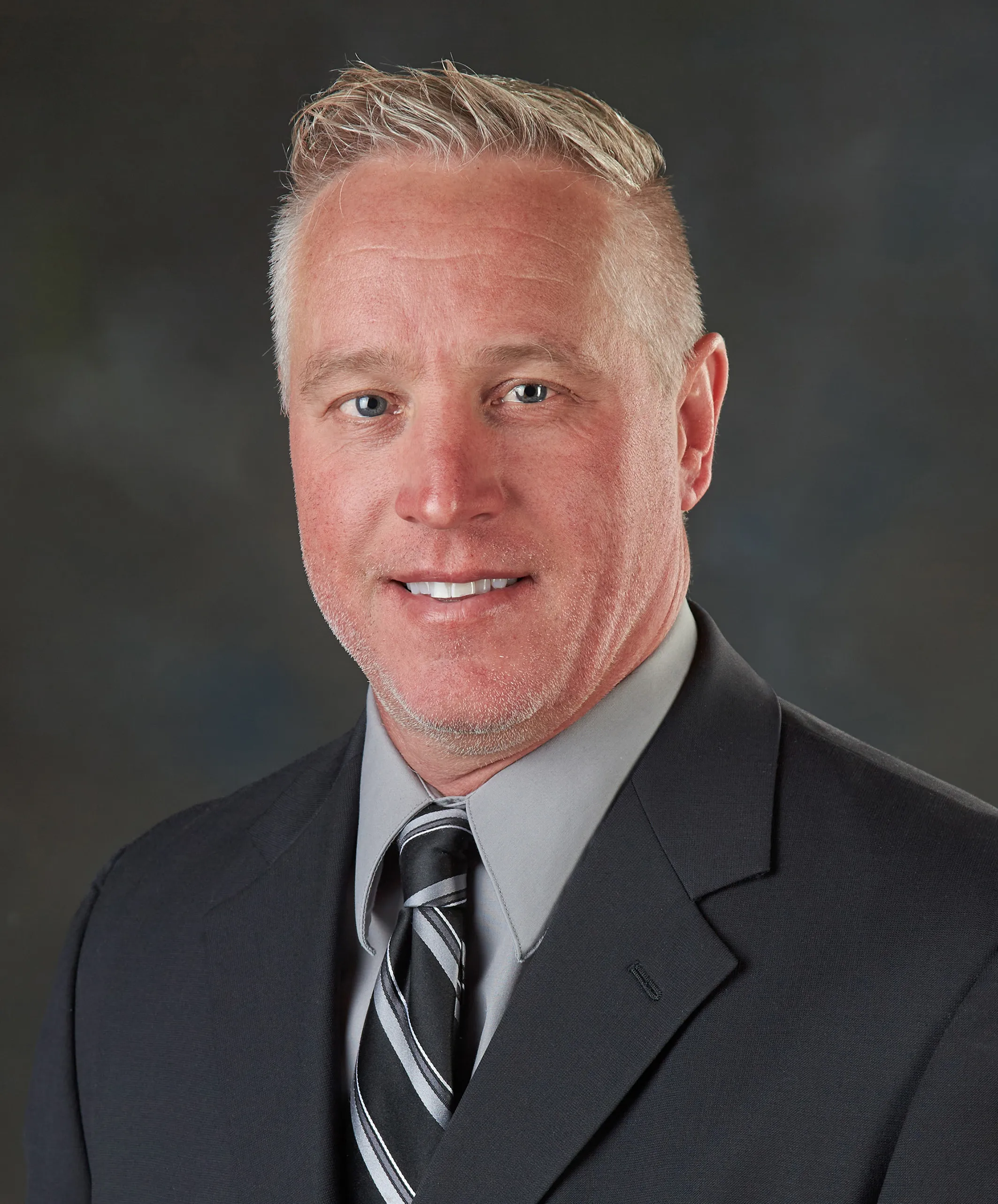 Bryan Woodhouse in portrait photo with dark blazer, striped tie.